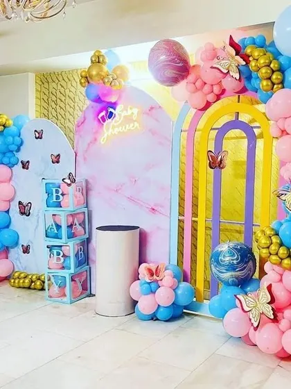 A colorful baby shower with pastel pink and blue balloons, butterfly accents, and modern arched backdrops.