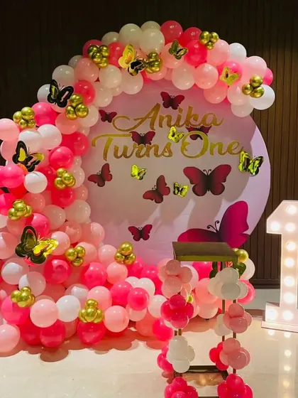 A pink and gold butterfly-themed first birthday party with a circular backdrop and a '1' marquee light.