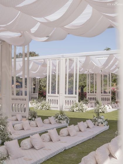 Low-level floor seating for guests, arranged under a canopy of flowing white fabric. This traditional seating style was given a modern twist with clean lines and plush white cushions.