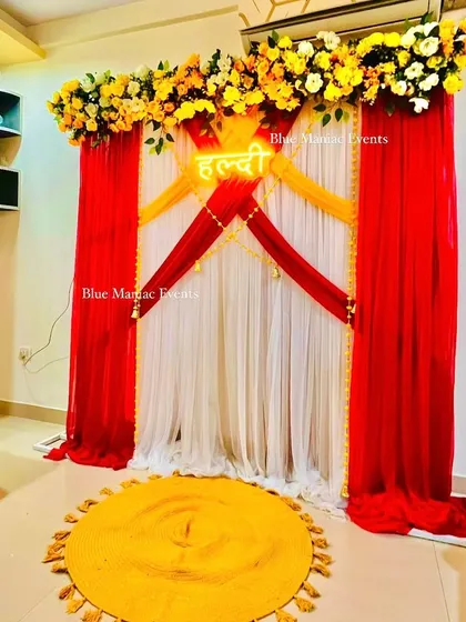 A bold and beautiful Haldi backdrop with red, yellow, and white drapes and a floral top border.