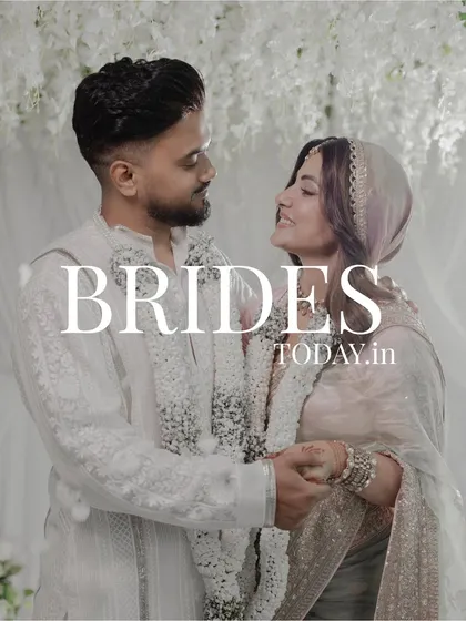 A feature in Brides Today, capturing the couple's loving gaze. The decor, with its layers of white florals, provides a timeless and romantic setting for their union.