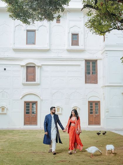A couple walks hand-in-hand on the lawns of a Patiala palace, with geese wandering around them, creating a charming scene.