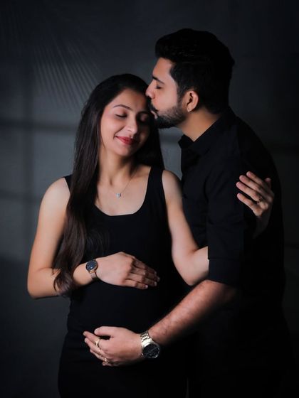 An intimate and moody studio portrait of an expecting couple. The dramatic low-key lighting creates a timeless and emotional image focused on their connection.