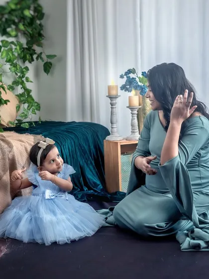 A sweet interaction between a mother and her daughter during a maternity shoot. The daughter looks up at her mom, creating a candid and heartwarming moment in the boho-chic setting.
