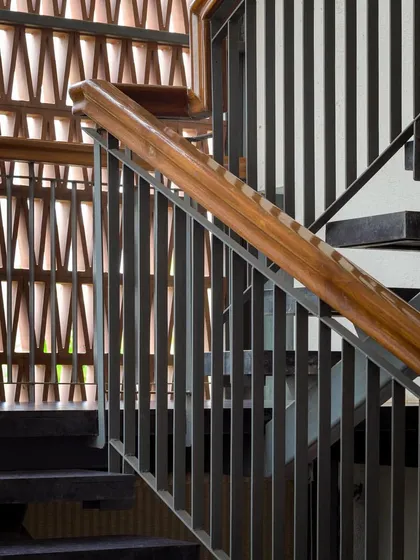 A close-up of the staircase reveals a careful composition of materials, with a wooden handrail, steel balusters, and a patterned brick jali wall.