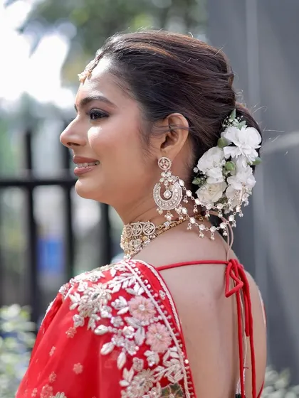 The complete look from the back, showcasing the elegant bridal bun adorned with fresh white flowers. This hairstyle complements the intricate embroidery on her red lehenga and keeps the focus on her glowing profile.