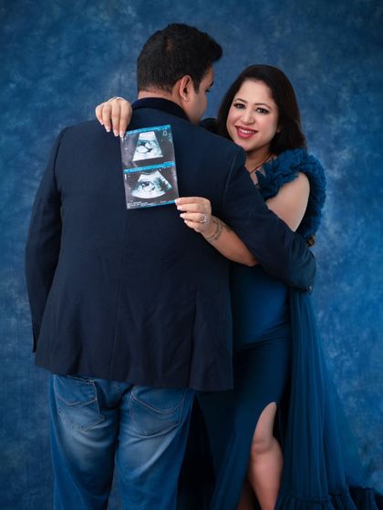 A creative and playful pose showing the sonogram, the first picture of their baby. The mother-to-be peeks over her husband's shoulder with a joyful smile.