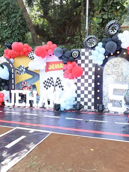 A full view of the car-themed birthday party setup, with a racetrack floor, checkered flag details, and character cutouts from the movie 'Cars'.