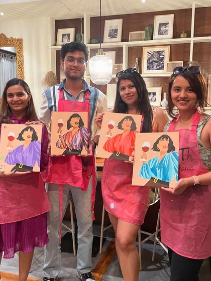 A group of four friends with their finished portraits from a wine and paint session. It's a great way to unwind and catch up.