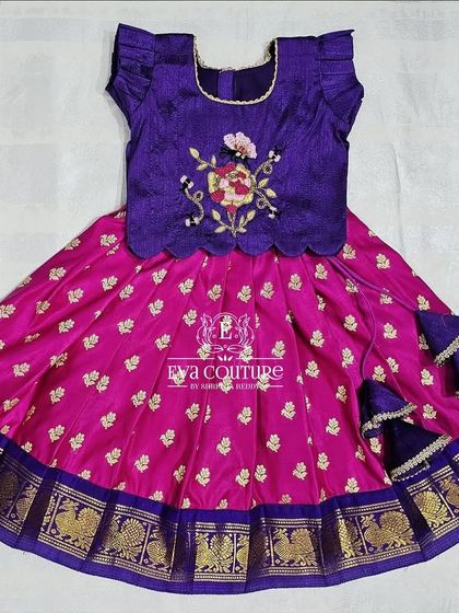A beautiful purple and pink pattu pavadai for newborns. The purple blouse has delicate floral embroidery, and the outfit includes extra margins for extended wear.