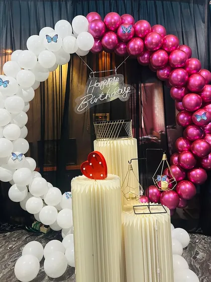 A lovely birthday setup with a pink and white balloon arch decorated with small butterflies. The lit-up heart prop adds a touch of sweetness to the design.