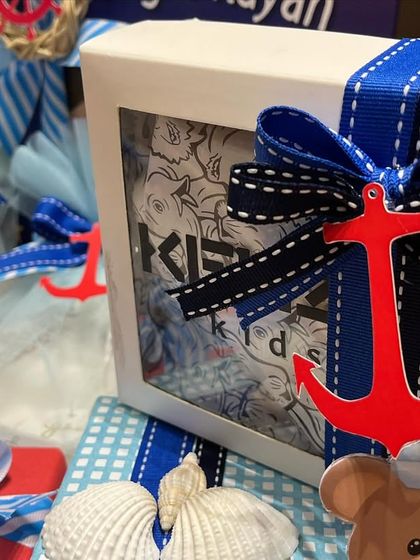 A close-up of the nautical details from a baby boy hamper. The red anchor charm, striped ribbon, and seashell accents perfectly capture the little sailor theme.