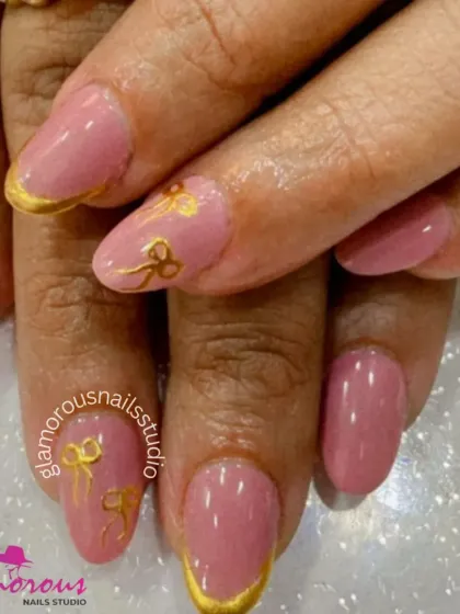 Tied with a golden bow. This sweet and elegant manicure features a soft pink base, gold French tips, and delicate, hand-painted golden bows.