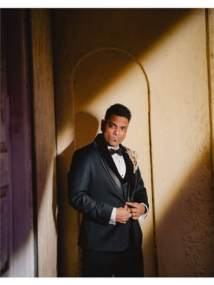 A stylish groom portrait using dramatic lighting. The play of light and shadow against the wall creates a moody and sophisticated image.
