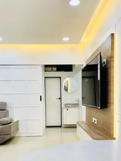 A glimpse into a finished living room where different areas are connected. The design features a custom TV unit with backlighting, a comfortable sectional sofa, and a clear view into the modern washbasin area, showing how we create a cohesive flow.