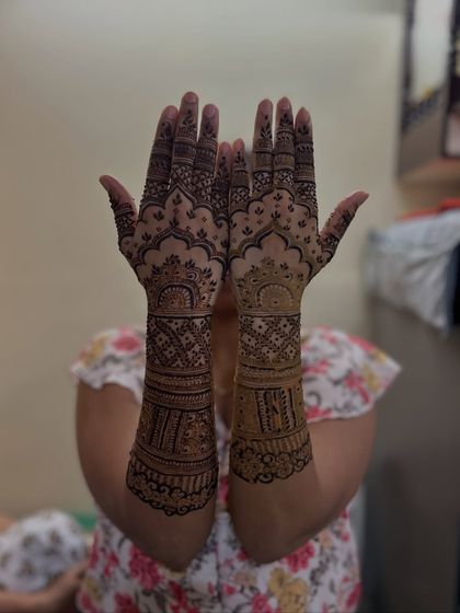A classic and symmetrical bridal mehendi design. Both hands are adorned with intricate patterns, including domes and detailed linework that extends from the fingers to the forearms.