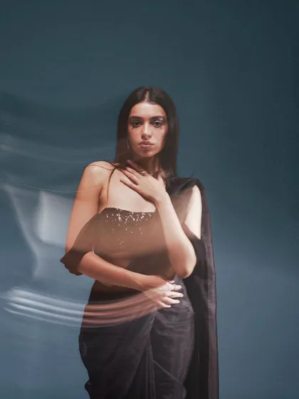 A creative portrait using a slow-shutter drag technique. The motion blur effect adds a dreamy, ethereal quality to this image of a modern black saree.