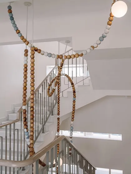 A view of the LUNA installation from the top of the staircase. The loops and drapes of the beads create a playful, sculptural form against the clean white walls of the penthouse.