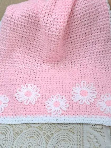 For a pretty-in-pink nursery, this blanket is made in a soft pink with a white border and is decorated with five white daisy flowers.
