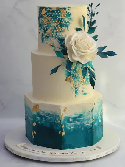 A bold and artistic choice for a modern wedding. This three-tiered cake features a hand-painted watercolor effect in shades of teal, accented with edible gold leaf and a single, striking white sugar rose.