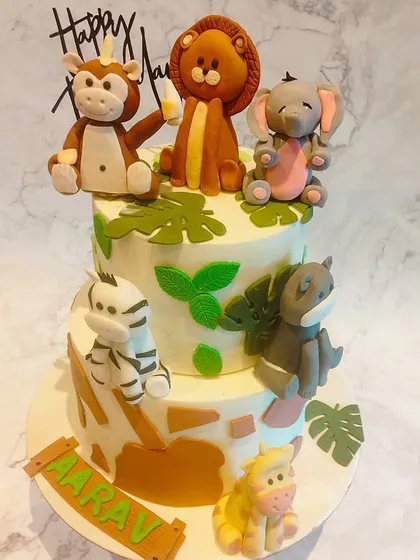 A cute two-tiered jungle animal cake for a little one's birthday. It's decorated with fondant leaves and adorable, hand-molded figures of a lion, monkey, elephant, and zebra.