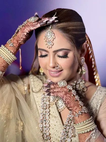 A close-up of a bride in a beautiful beige-gold outfit. The heavy, layered Polki and diamond jewellery set, complete with a large hathphool, creates a look of pure luxury.