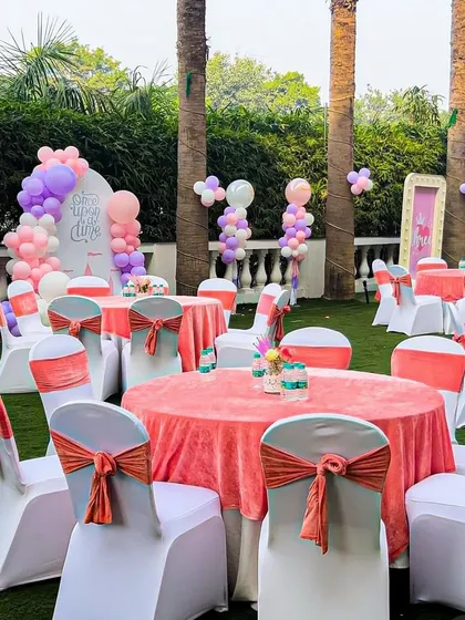 Guest tables at the princess party, decorated with pink tablecloths and coral chair sashes. The balloon decorations in the background tie the whole look together.
