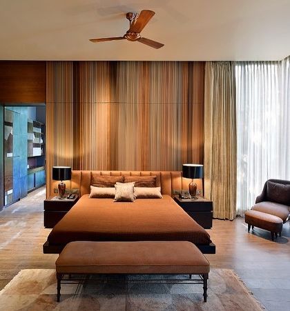 This bedroom is a cocoon of warmth and texture. A custom-paneled wall in varying shades of wood creates a stunning backdrop for the bed, while floor-to-ceiling sheer curtains diffuse the light, adding to the room's serene quality.