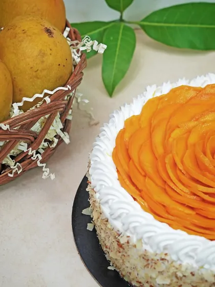 A whole mango cake with intricately arranged mango slices on top, next to a basket of fresh mangoes. This shot connects the final product to its fresh, natural ingredients.