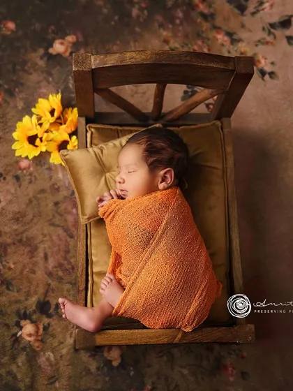 An autumnal feel with this newborn nestled in a wooden bed prop, wrapped in a cozy orange blanket and accented with sunflowers.