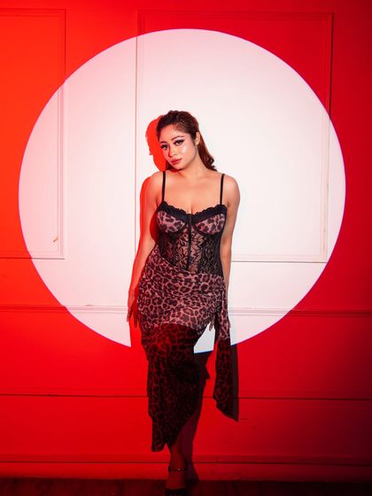 A high-concept studio shot with model Anuja. The dramatic red background and circular spotlight create a theatrical and bold fashion statement.