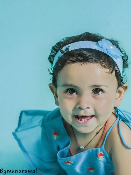 A simple and sweet close-up portrait of a toddler against a soft blue background, her curious eyes and gentle smile making for a perfect, timeless memory.