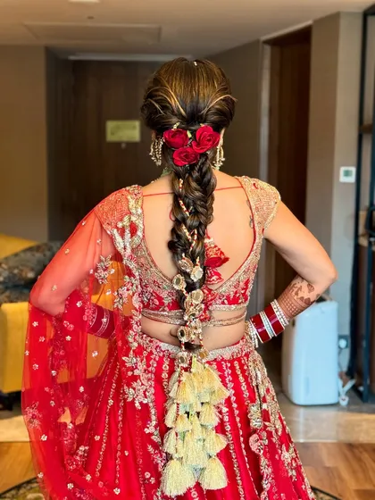 This is a quintessential Indian bridal look, featuring a thick, traditional braid adorned with red roses and intricate gold tassels (parandi). This hairstyle is designed to perfectly match a classic red lehenga, making it ideal for the main wedding ceremony.