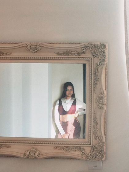 A quiet, sun-kissed moment captured in a mirror. This shows a layered look with a bralette over a white shirt, playing with textures and silhouettes for an artistic feel.