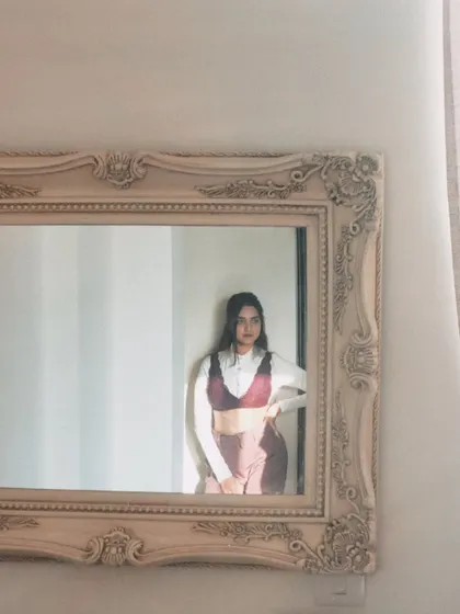A quiet, sun-kissed moment captured in a mirror. This shows a layered look with a bralette over a white shirt, playing with textures and silhouettes for an artistic feel.