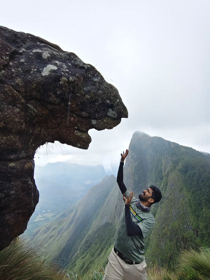 A fun, creative photo of a trekker interacting with a lion-shaped rock formation in Munnar.