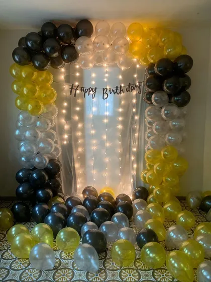 This is a complete birthday photo booth setup with a balloon arch in yellow, black, and clear balloons. The fairy light curtain in the background ensures great pictures day or night.