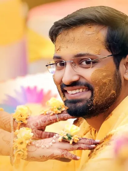 A close-up of the groom during his haldi ceremony, his face smeared with turmeric and a bright, happy smile on his face.