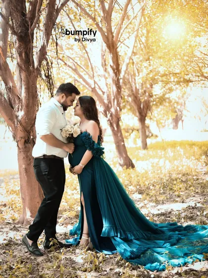 A romantic outdoor maternity portrait of a couple, bathed in the soft golden hour light. The way her teal gown flows in the gentle breeze adds a touch of fairytale magic to their special moment.