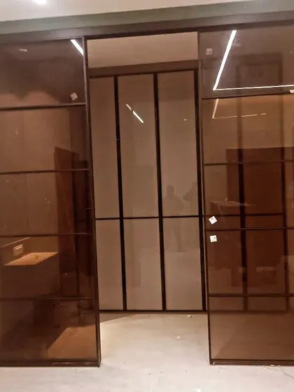 These large, floor-to-ceiling sliding glass doors create a dramatic entrance to a walk-in closet. The bronze-tinted glass and black metal frame offer an industrial-luxe aesthetic.
