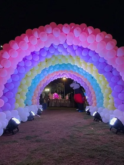 A rainbow balloon arch tunnel in a garden, creating a fairytale entrance for a princess-themed birthday party.