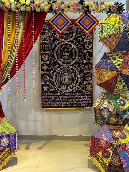 A creative entrance decoration using colorful drapes and stacked Rajasthani umbrellas. The traditional wall hanging adds an artistic touch to the setup.