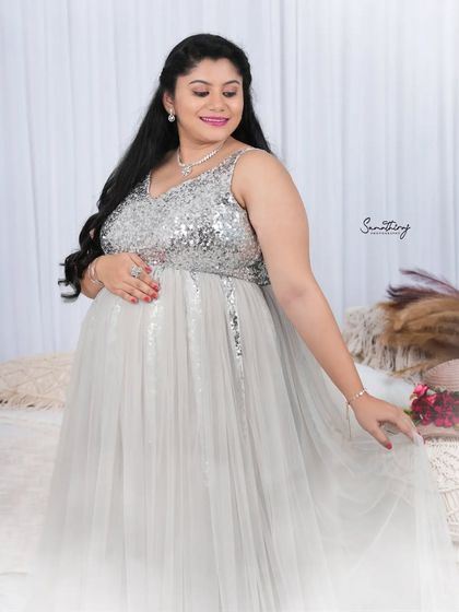 A serene portrait of a mother-to-be in a silver sequined gown. The soft lighting and boho-chic decor create a peaceful and stylish indoor setting.