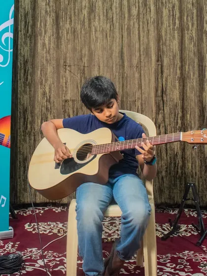 A student plays his acoustic guitar in front of our "Open Mic Session" banner at the HSR branch.