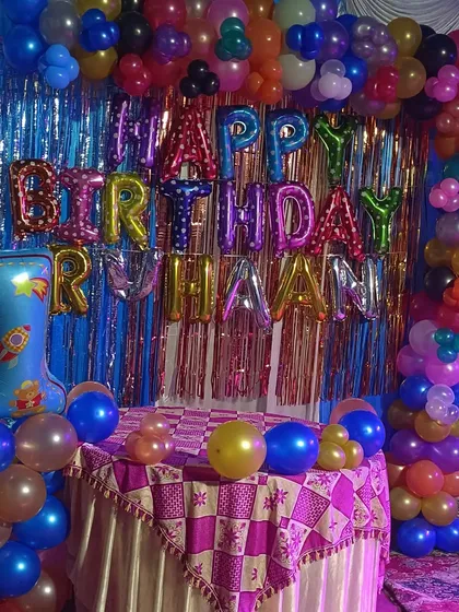 A colorful first birthday decoration with a full balloon arch and table setup. The multicolor foil "Happy Birthday" balloons add an extra pop of fun.