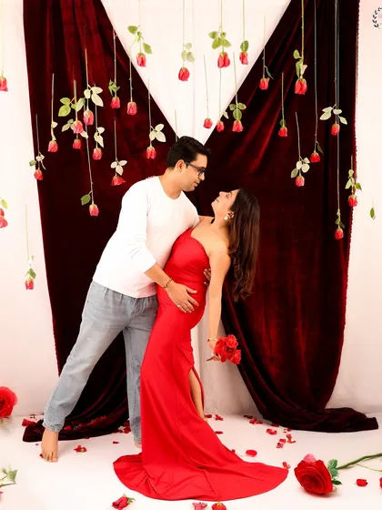 A playful and romantic pose from a Valentine's maternity shoot. The couple shares a dance amidst falling rose petals, capturing the joy and love of their journey together.