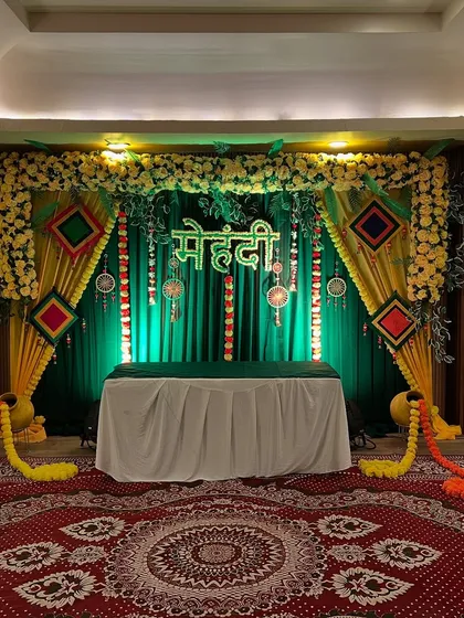 A classic Mehendi setup with a green and yellow backdrop, floral arrangements, and traditional hangings, perfect for creating a festive vibe.