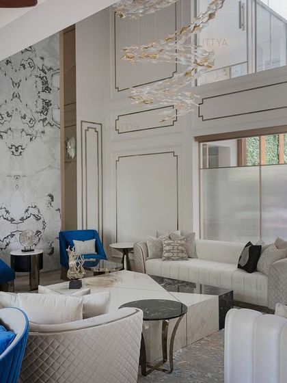 Another view of the poolside living area, highlighting the classic wall paneling and a modern, sculptural chandelier. The arrangement of quilted and tufted sofas in neutral tones creates an elegant and comfortable space for gathering.