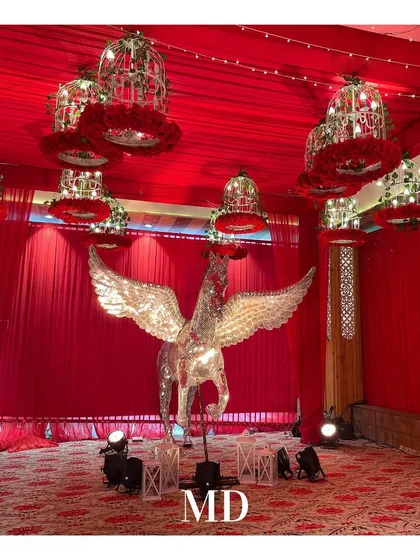 A unique decor element for a fantasy-themed engagement. A life-sized, winged horse statue made of mirrors stands as a centerpiece, surrounded by hanging bird cages filled with red roses.