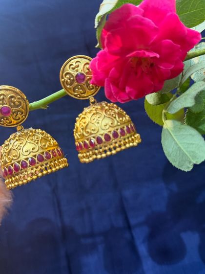Classic temple jewellery style jhumkas. These gold earrings with intricate heart motifs and red stones are a timeless accessory.